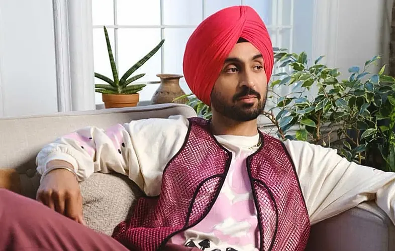  Diljeet Dosanjh wearing a pink turban and a stylish vest sits comfortably on a couch.
