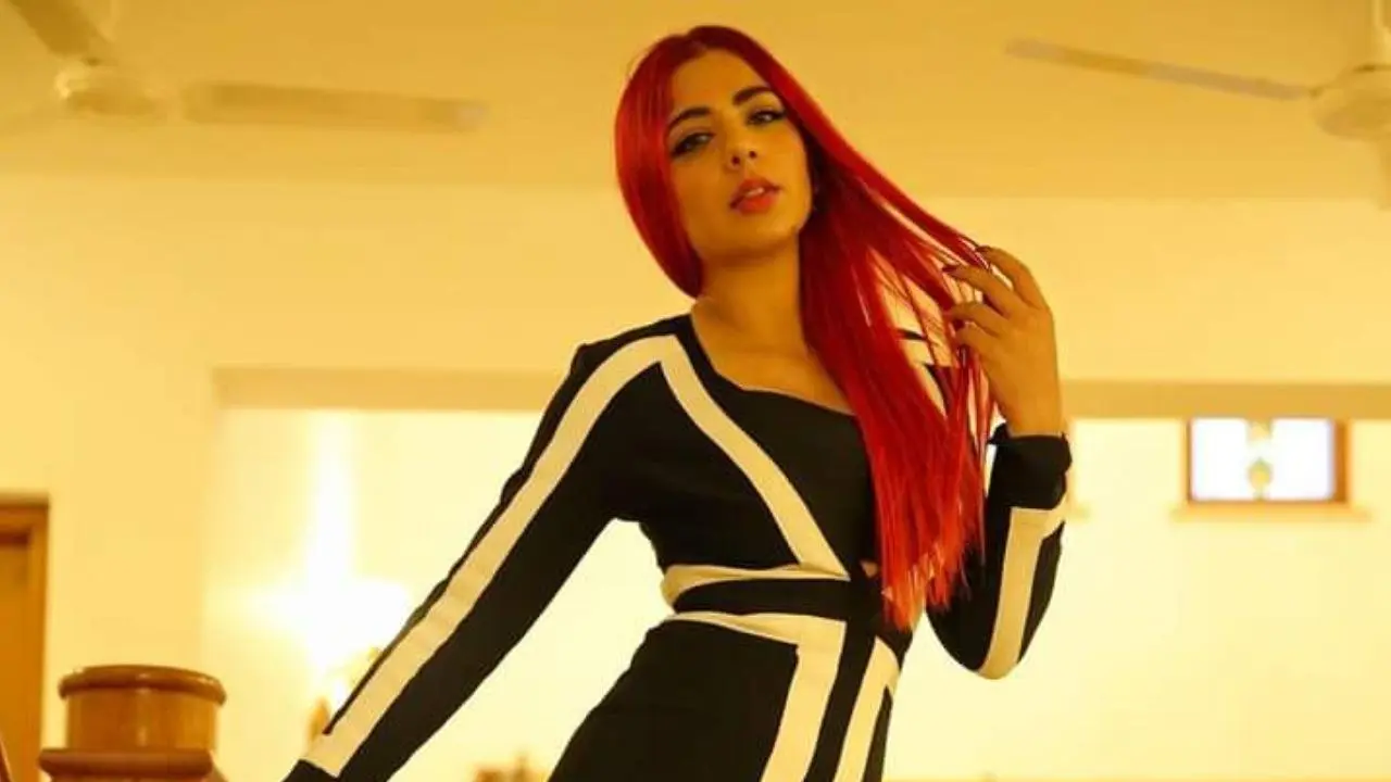 Singer Jasmine Sandlas with vibrant red hair, wearing a black and white striped dress.