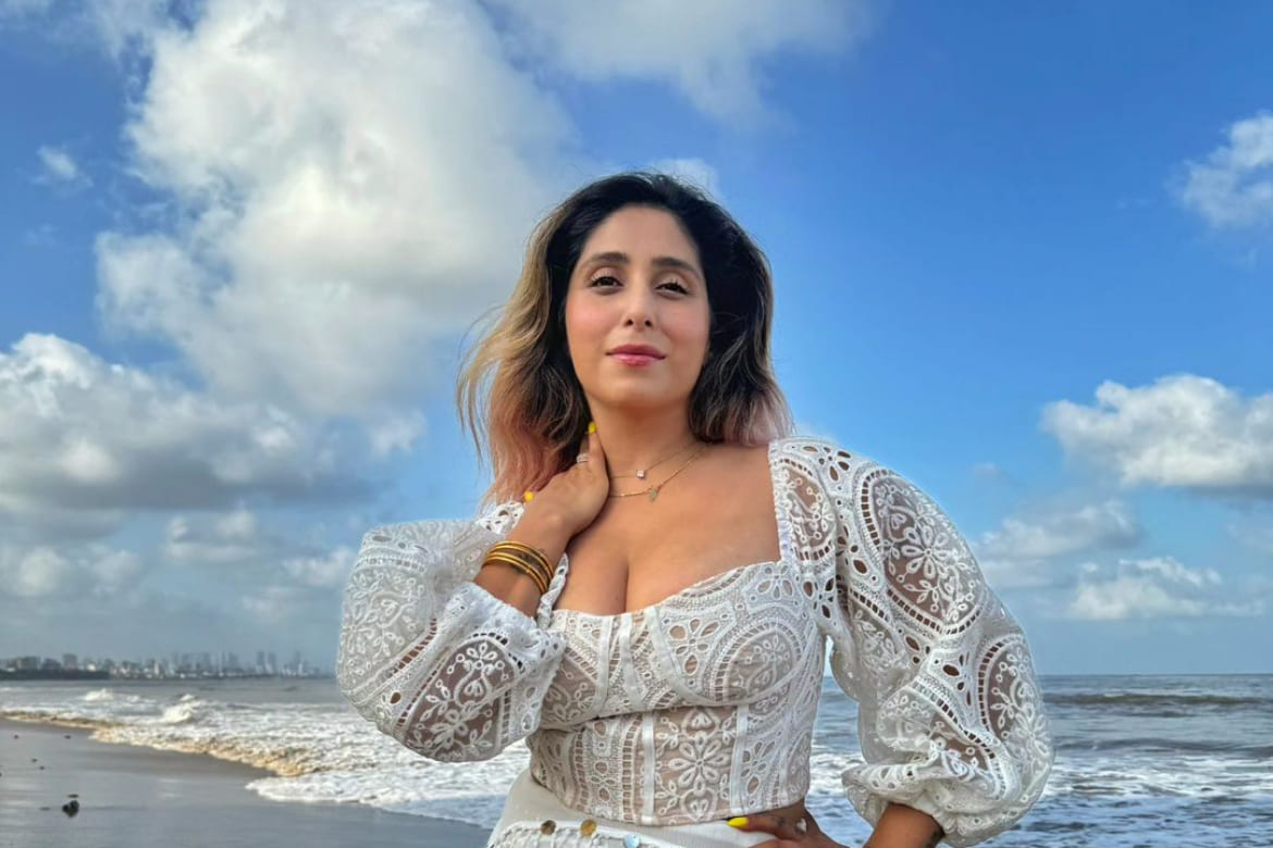 Singer Neha Bhasin in a white lace top posing on a beach.
