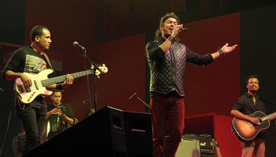 Papon performing on a stage bathed in warm, red light, with a lead singer gesturing to the audience and other members playing instruments