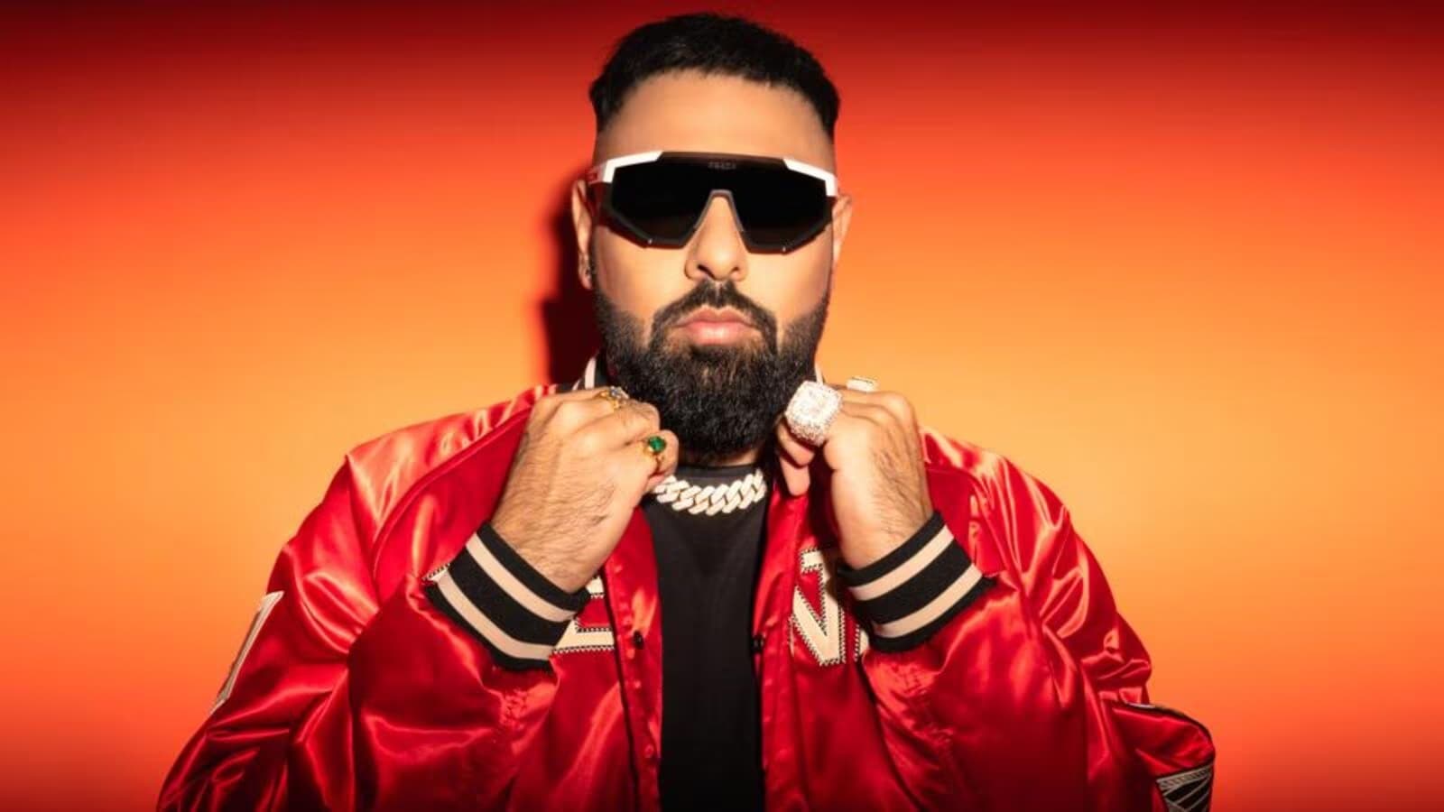 Image of Badshah, with an orange background staring directly into the camera in a red jacket.